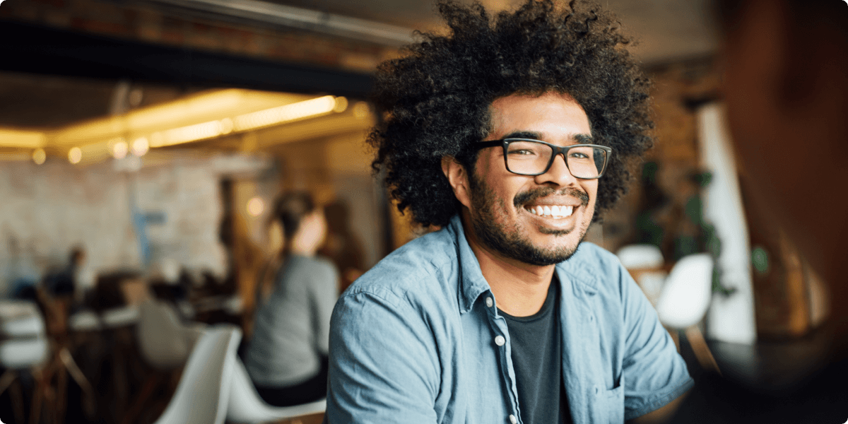 A man with glasses gives a broad smile in a cafe.